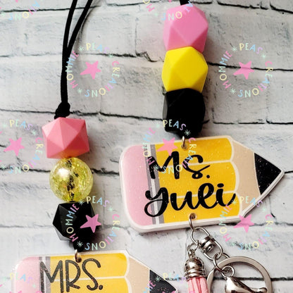 Mommie Peas Creations personalized glitter pencil lanyard with pink, yellow, and black beads, and a pink tassel. Features a holographic glitter pencil charm with custom text.