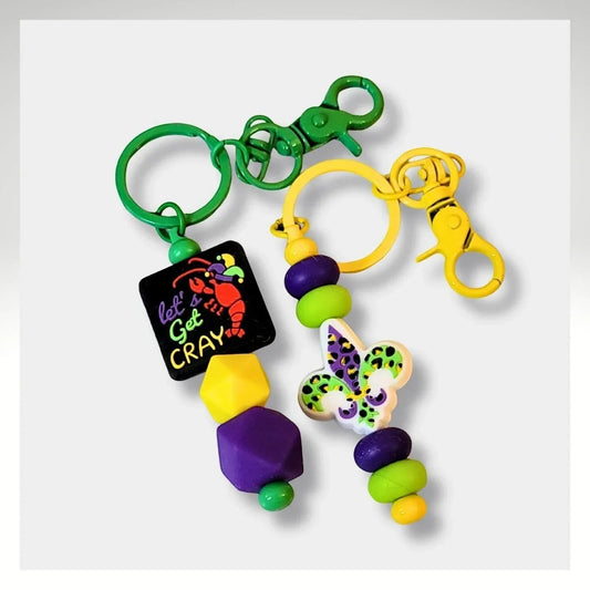 Mommie Peas Creations Mardi Gras beaded keychains with crawfish and fleur-de-lis charms in purple, green, and gold.