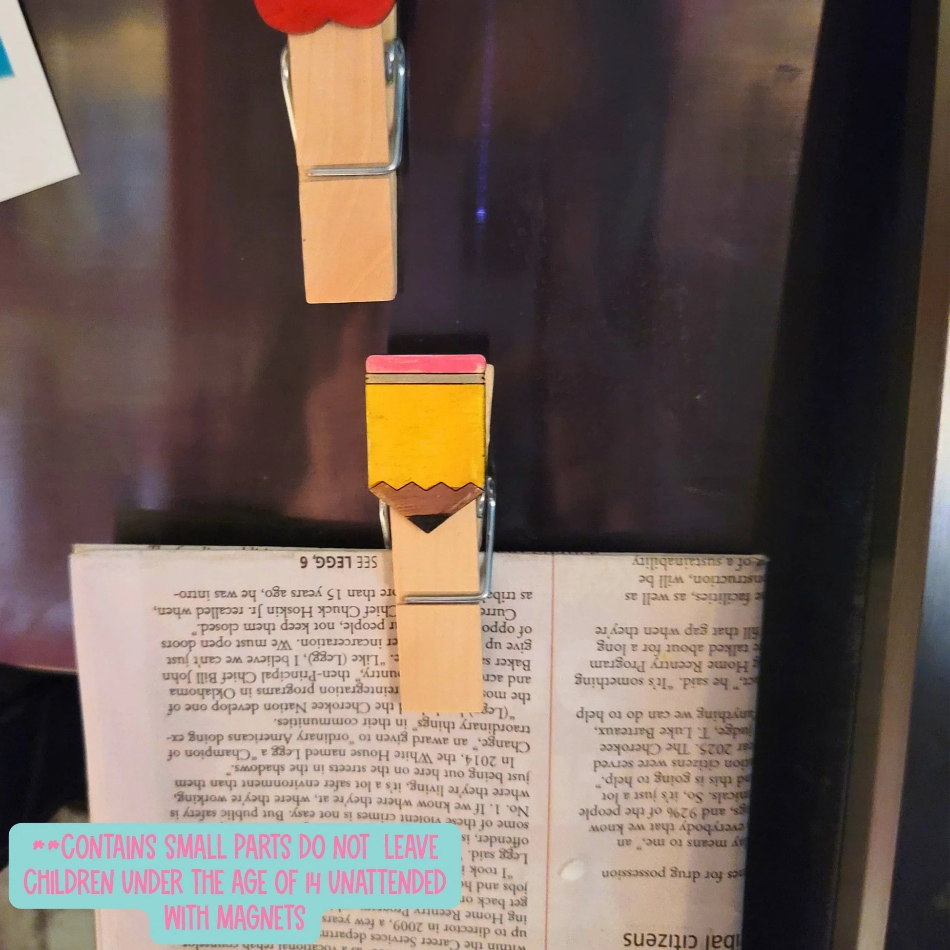 Mommie Peas Creations hand-painted wooden clothespin shaped like a pencil with pink eraser and yellow body, holding a book.