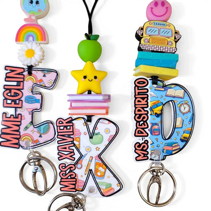 Colorful handmade teacher lanyards with personalized names, rainbow, apple, star, and school bus charms from Mommie Peas Creations