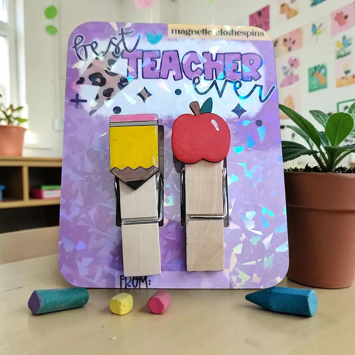 Mommie Peas Creations hand-painted wooden magnetic clothespins featuring a yellow pencil and red apple design on a purple holographic card that says "best TEACHER ever".