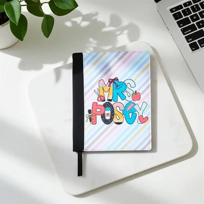 Mommie Peas Creations personalized teacher padfolio with colorful "Mrs. Posey" text and school supplies on a pastel striped background.