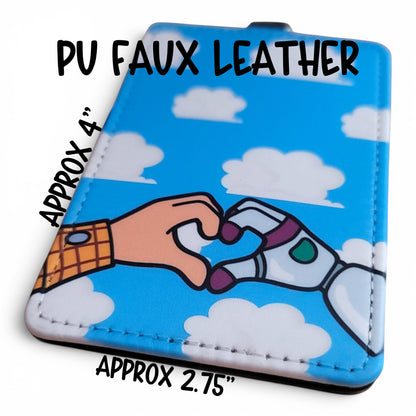 Mommie Peas Creations Toy Story inspired PU leather ID holder with Woody and Buzz heart hands on a cloudy blue sky.