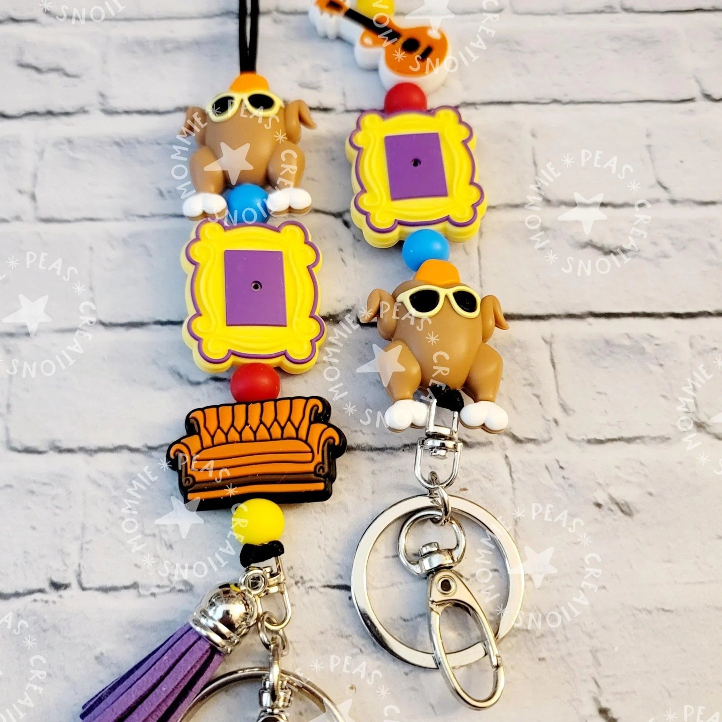 Mommie Peas Creations Fall Turkey Lanyard with Friends-themed charms: a turkey with sunglasses, a yellow picture frame, and an orange couch. Features purple tassel.