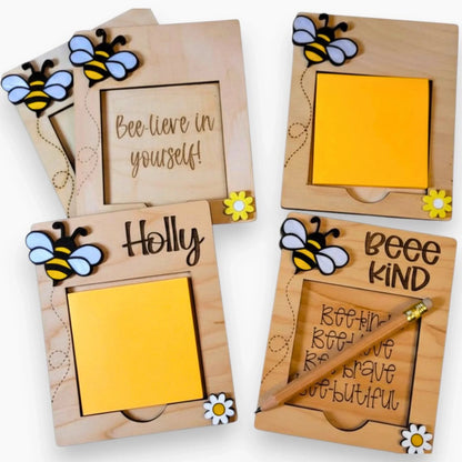 Handmade wooden notepad holders with yellow and black bee decorations, daisy accents, and uplifting engraved messages, perfect as personalized gifts.