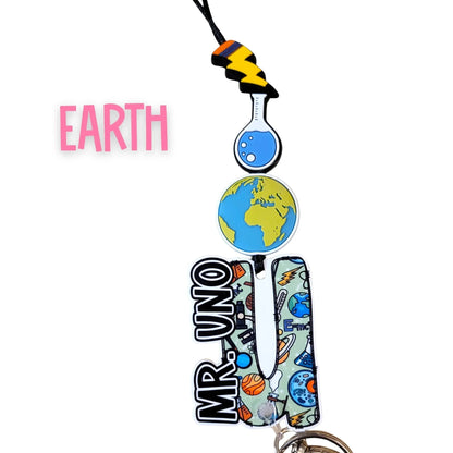Mommie Peas Creations Earth science lanyard with planet Earth, beaker, and lightning bolt charms. Features custom name plate.