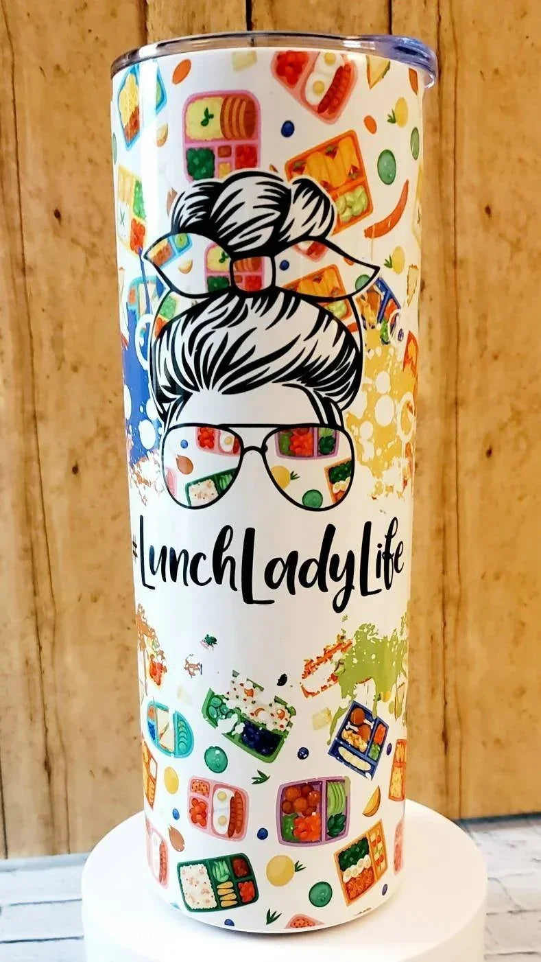 Mommie Peas Creations white 20 oz stainless steel tumbler with a graphic of a woman with messy bun and sunglasses reflecting lunchboxes, text #LunchLadyLife, and scattered lunchbox patterns.