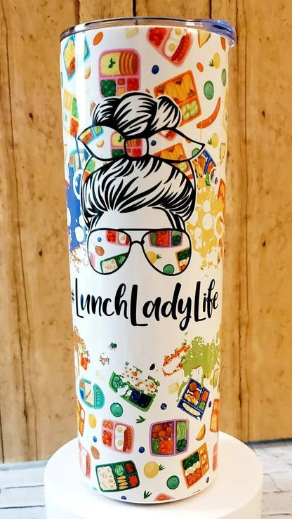 Mommie Peas Creations white 20 oz stainless steel tumbler with a graphic of a woman with messy bun and sunglasses reflecting lunchboxes, text #LunchLadyLife, and scattered lunchbox patterns.