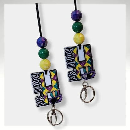 Mardi Gras initial lanyard with purple, green, and gold beads and a custom acrylic initial charm reading "MS. HAPPY".