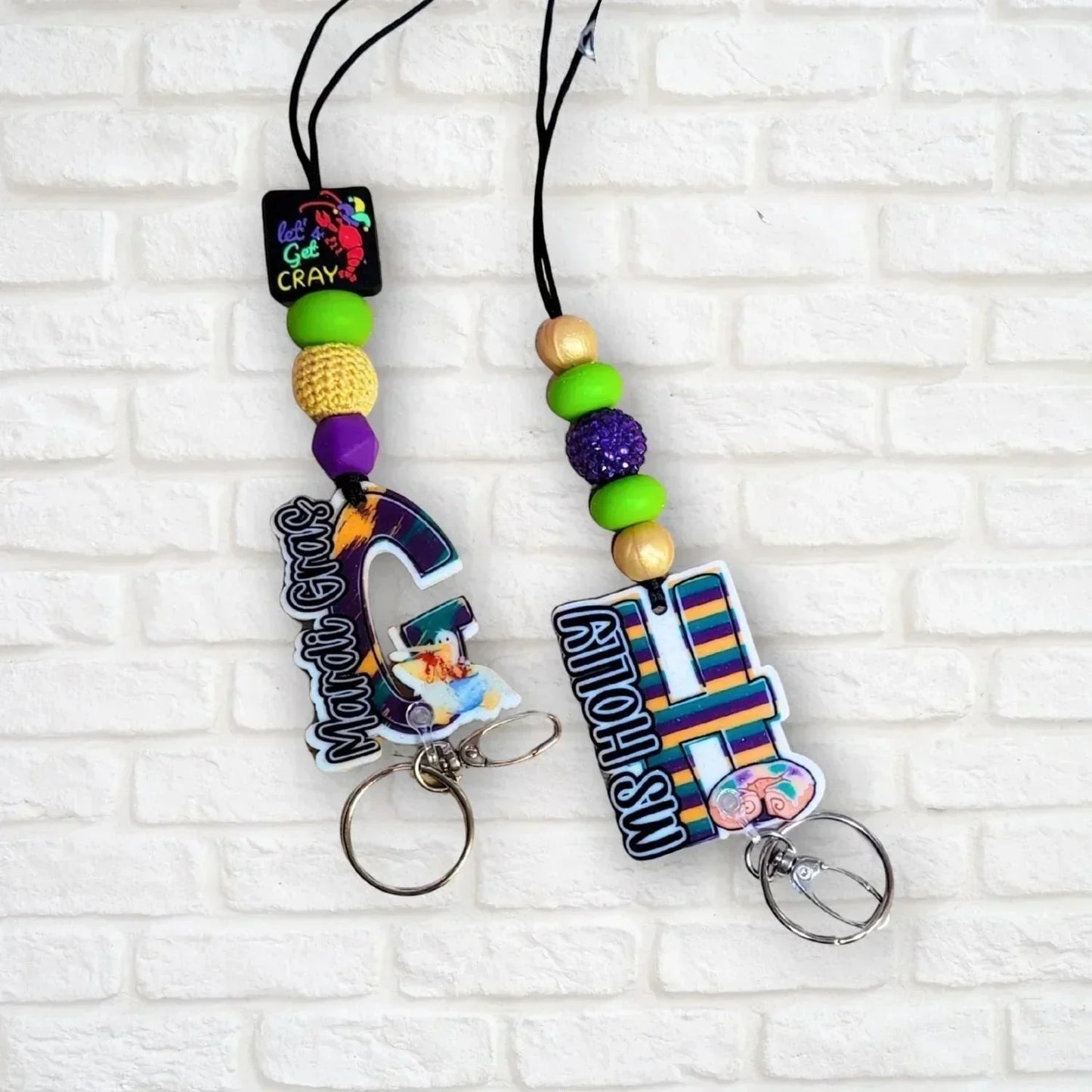 Mardi Gras initial lanyard with purple, green, and gold beads. Features custom acrylic initial charms and a lobster clasp. Mommie Peas Creations.