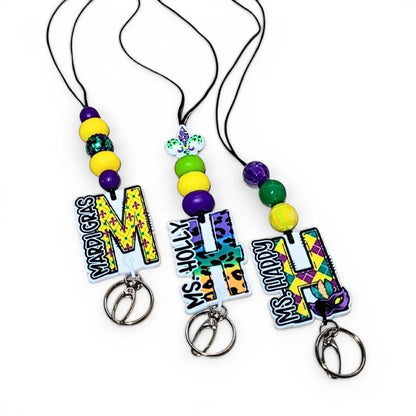 Mommie Peas Creations Mardi Gras initial lanyard with purple, green, and gold beads and custom acrylic initial charms.