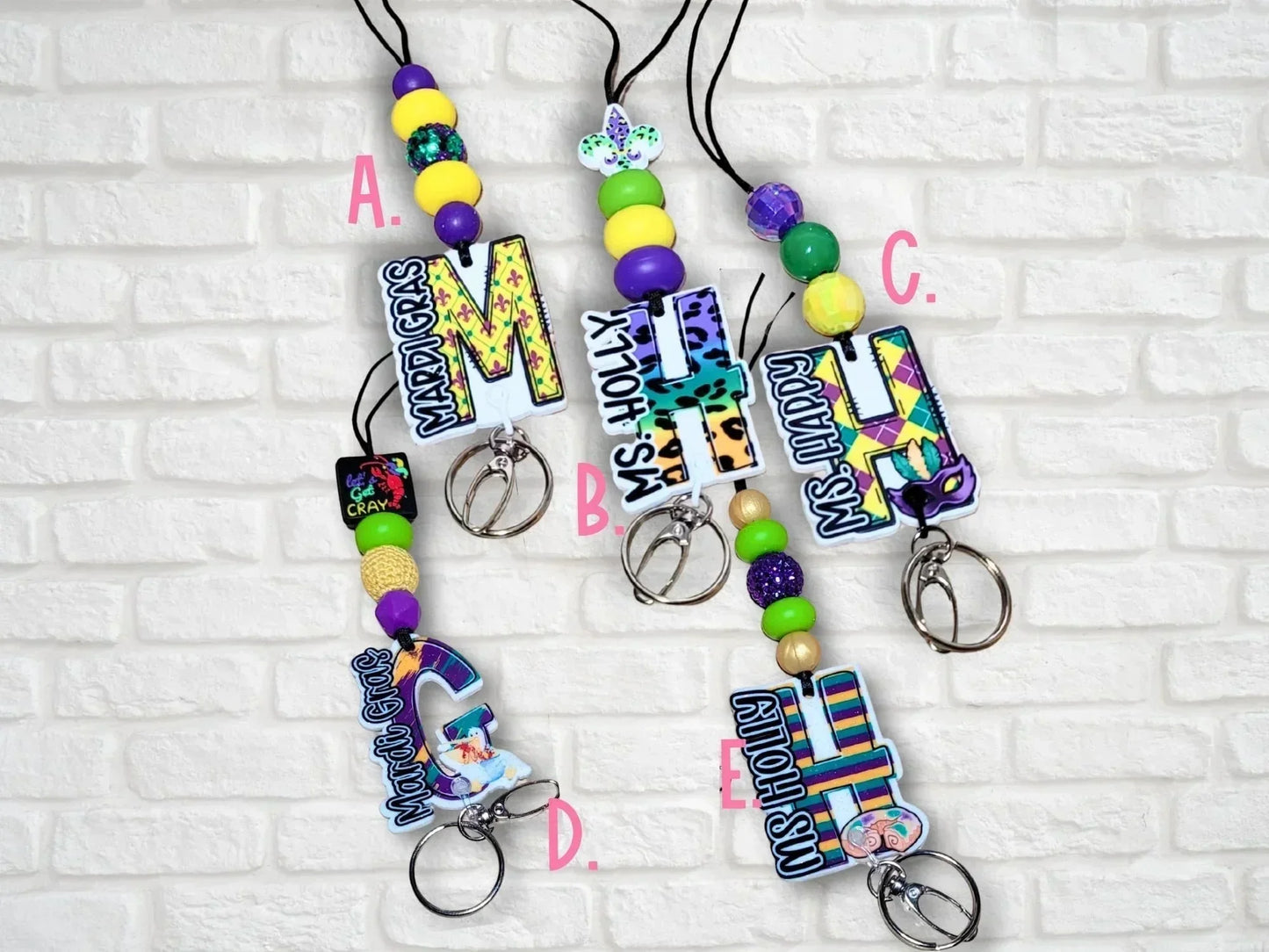 Mardi Gras themed lanyards from Mommie Peas Creations with personalized initial charms and colorful beads in purple, green, and gold.