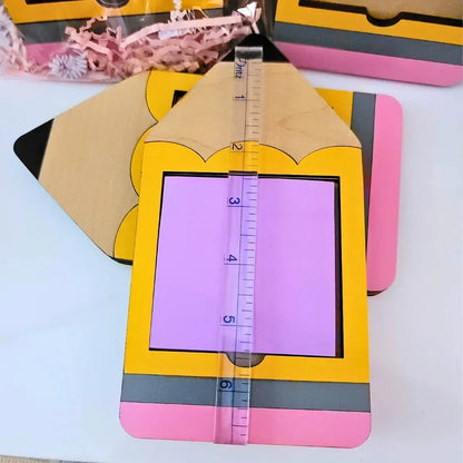 Mommie Peas Creations yellow, pink, and grey wooden pencil Post-it note holder with black tip. Holds 3x3 Post-it notes.