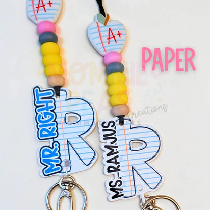 Mommie Peas Creations personalized teacher lanyard with silicone beads, acrylic charm shaped like a notebook paper apple, and custom letter charm.