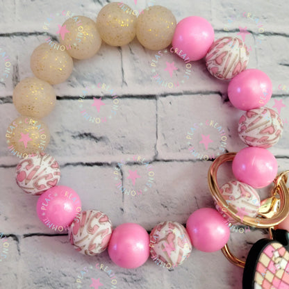 Mommie Peas Creations pink and gold glitter silicone wristlet keychain with pink apple charm and patterned beads.