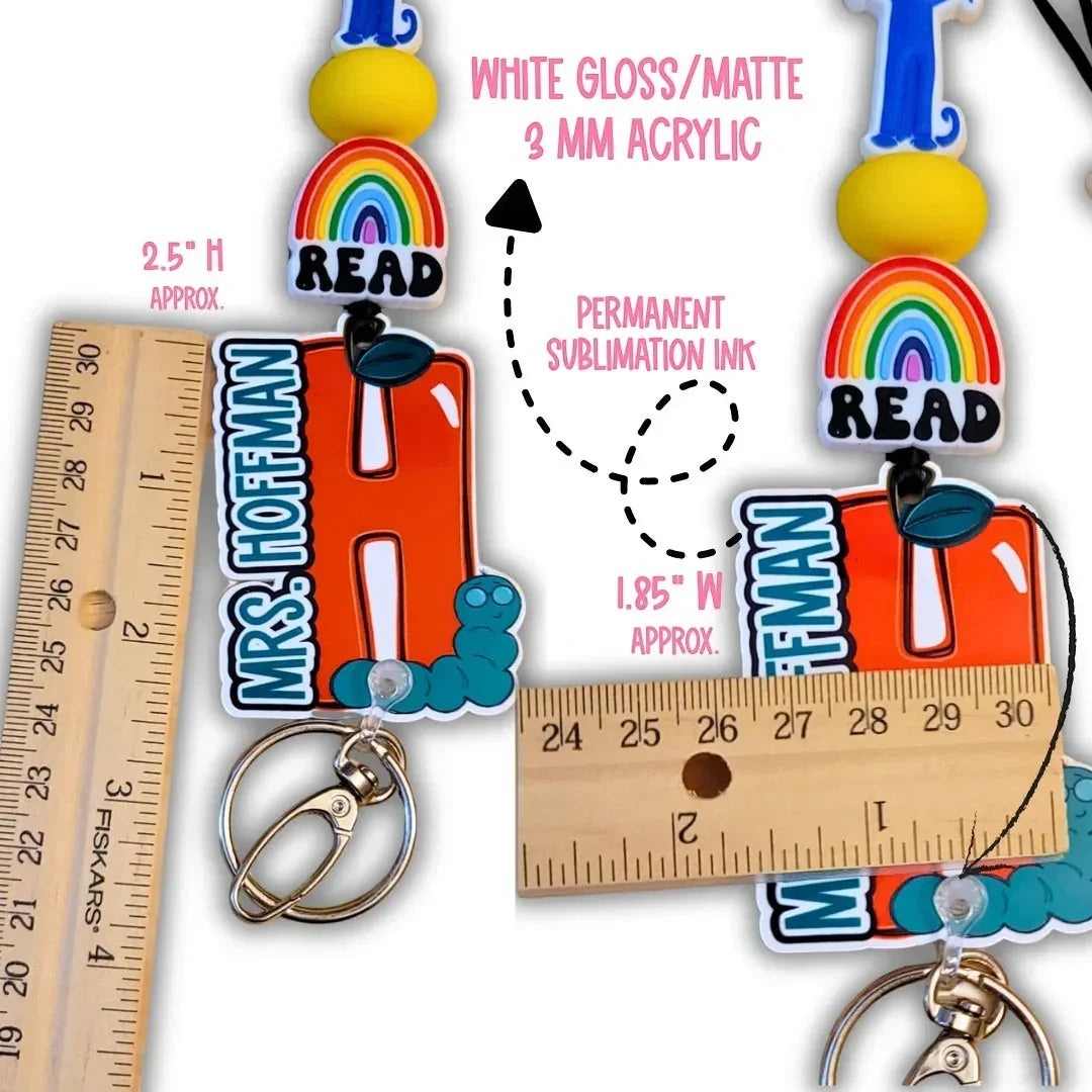 Mommie Peas Creations red apple lanyard with "READ" charm, personalized name, and caterpillar detail. Features breakaway clasp.