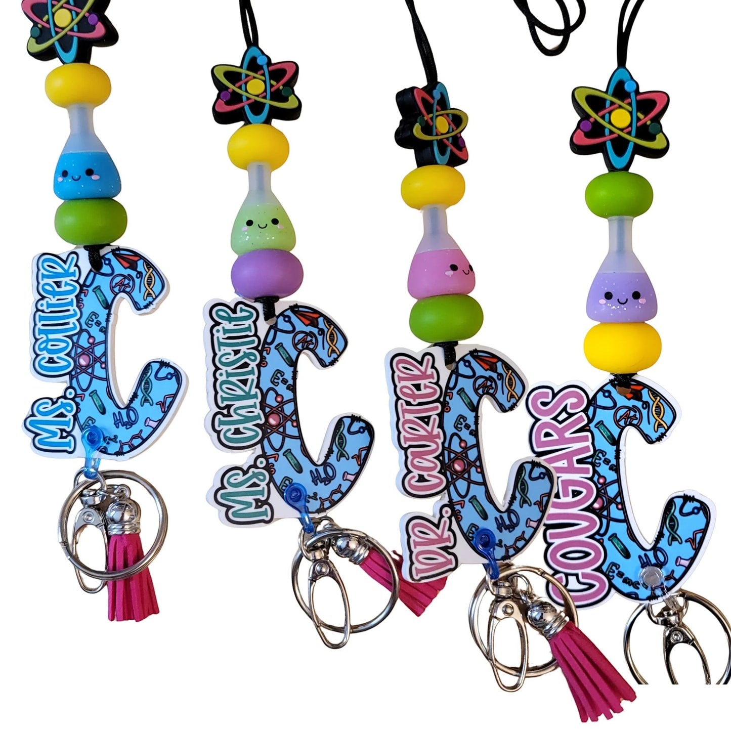 Mommie Peas Creations science lanyard with blue, green, yellow, and purple beads, featuring a science-themed acrylic initial and a pink tassel.
