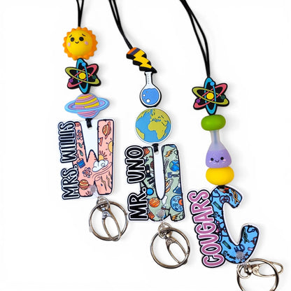 Mommie Peas Creations science lanyards with acrylic beads and charms: sun, atom, planet, earth, flask, and personalized letter charms with names like Mrs. Willis, Mr. Uno, and Cougars.