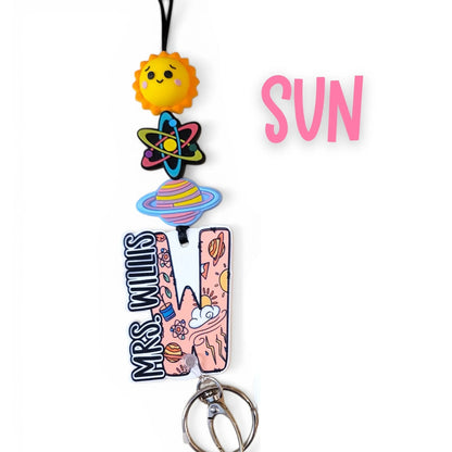 Mommie Peas Creations science lanyard with sun, atom, planet charms and personalized name plate. Features colorful silicone beads and a safety clasp.