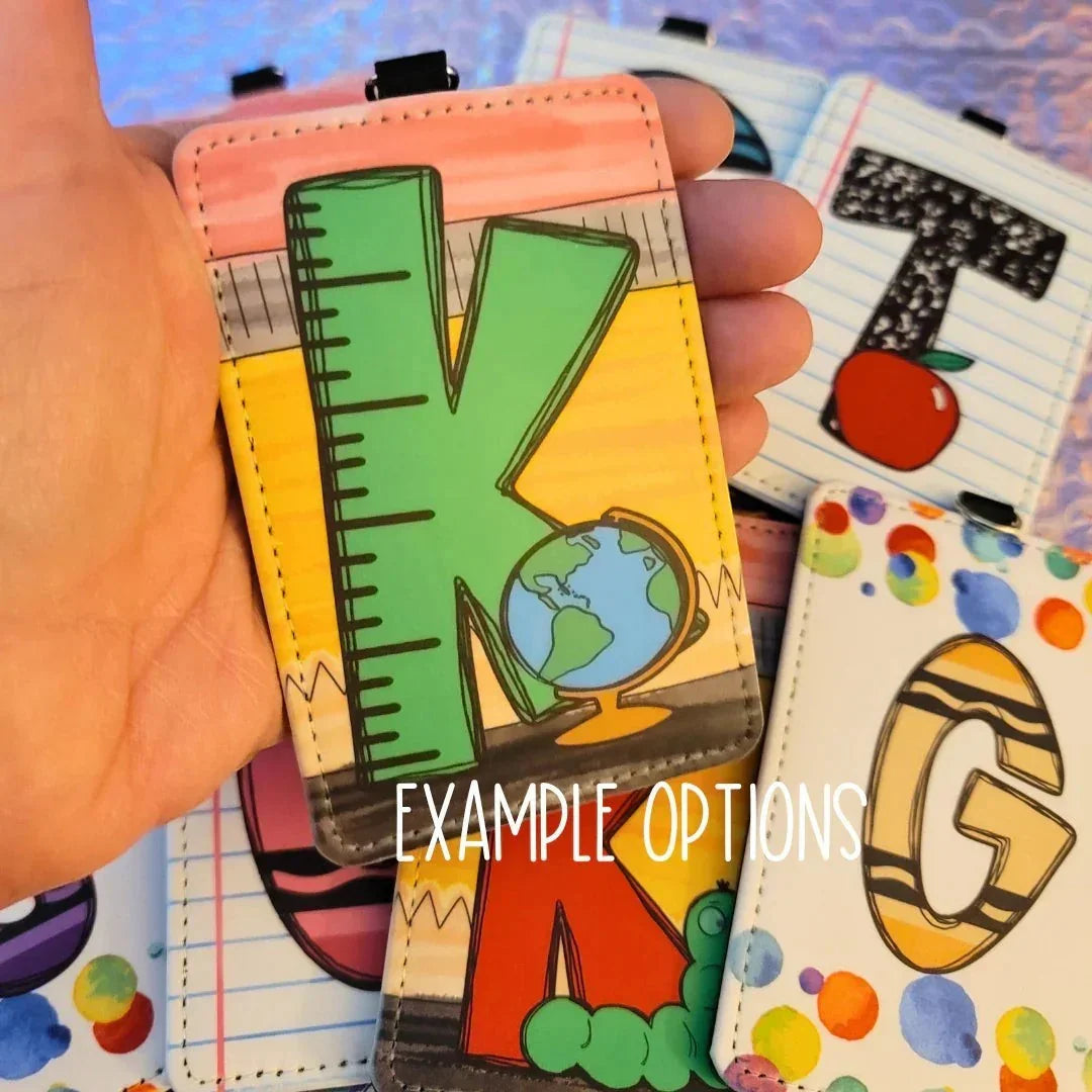 Mommie Peas Creations horizontal PU leather teacher badge holder with a green 'K' design, ruler, and globe. Features clear sleeve for ID.