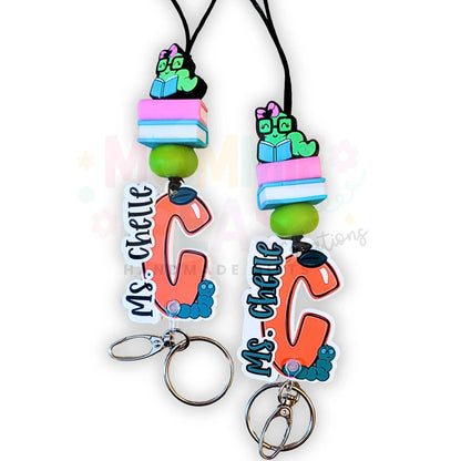 Mommie Peas Creations personalized teacher lanyard with orange letter C charm, green beads, and a cute worm on books charm.