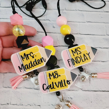 Mommie Peas Creations personalized teacher lanyard with glitter acrylic pencil charm, pink, yellow, and black beads, and retractable badge reel.