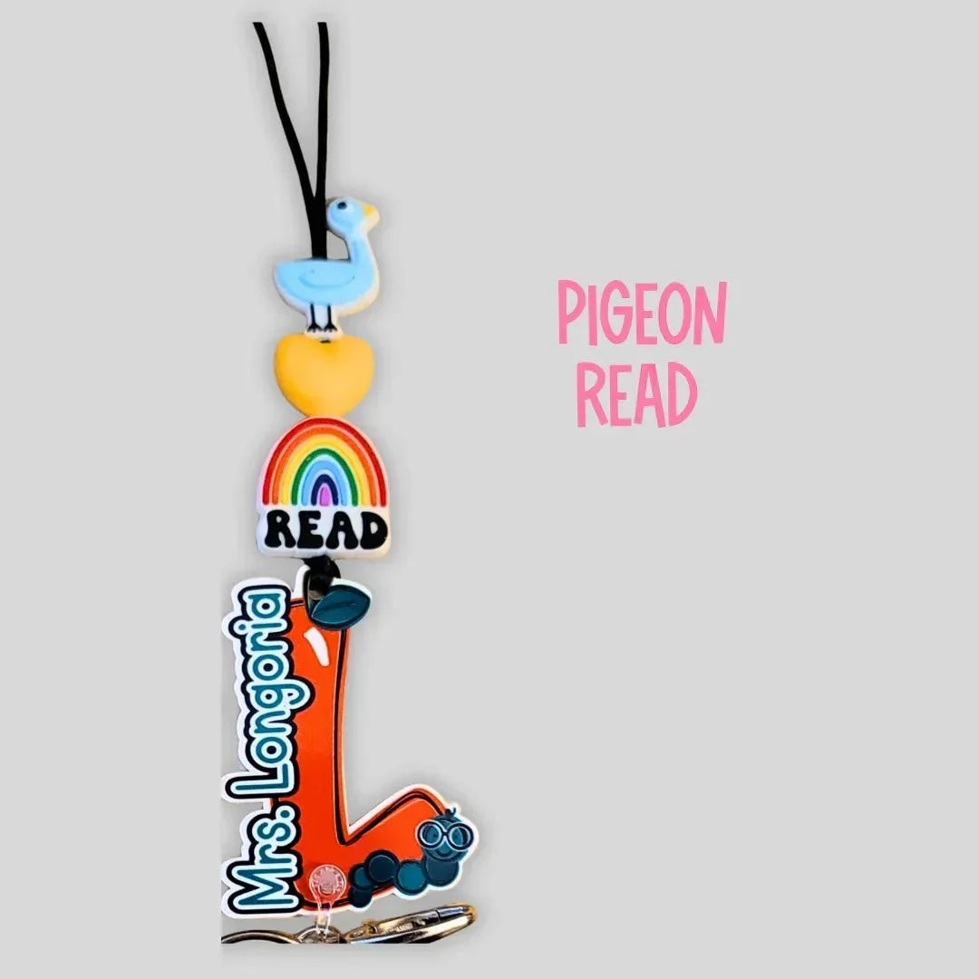 Mommie Peas Creations personalized lanyard with a blue duck, yellow heart, rainbow, and 'READ' charm, plus an orange 'L' charm with glasses and 'Mrs. Longoria' text.
