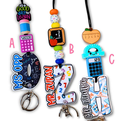 Mommie Peas Creations personalized teacher lanyard with silicone beads, acrylic charms, and custom letters. Features school-themed designs like calculators, apples, and rulers.